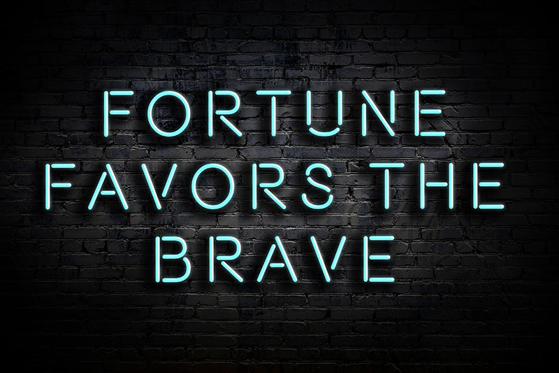 Fortune favors the brave blue text on black brick wall